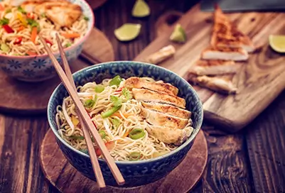 Bowl of ramen with chicken next to cutting board and fried rice bowl.