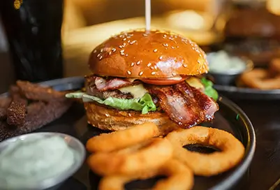 Burger with bacon, lettuce and tomato next to onion rings.